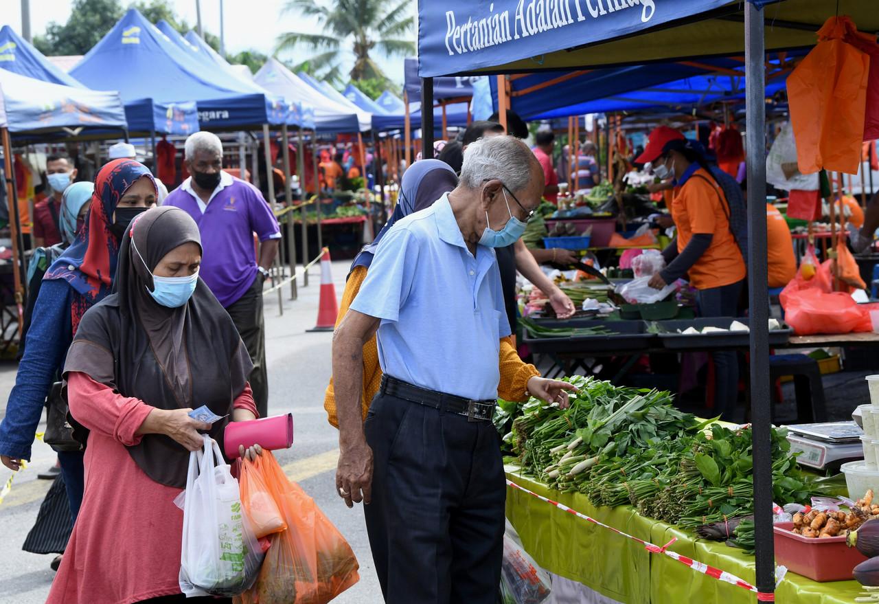Customers wearing face masks queue to buy vegetables at a stall at a farmers market in Seremban. Photo: Bernama