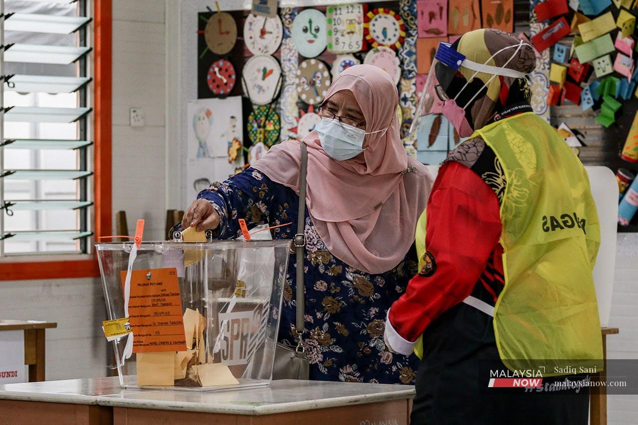 An Election Commission officer helps a voter cast her ballot at a polling station in Melaka for the recent state election.