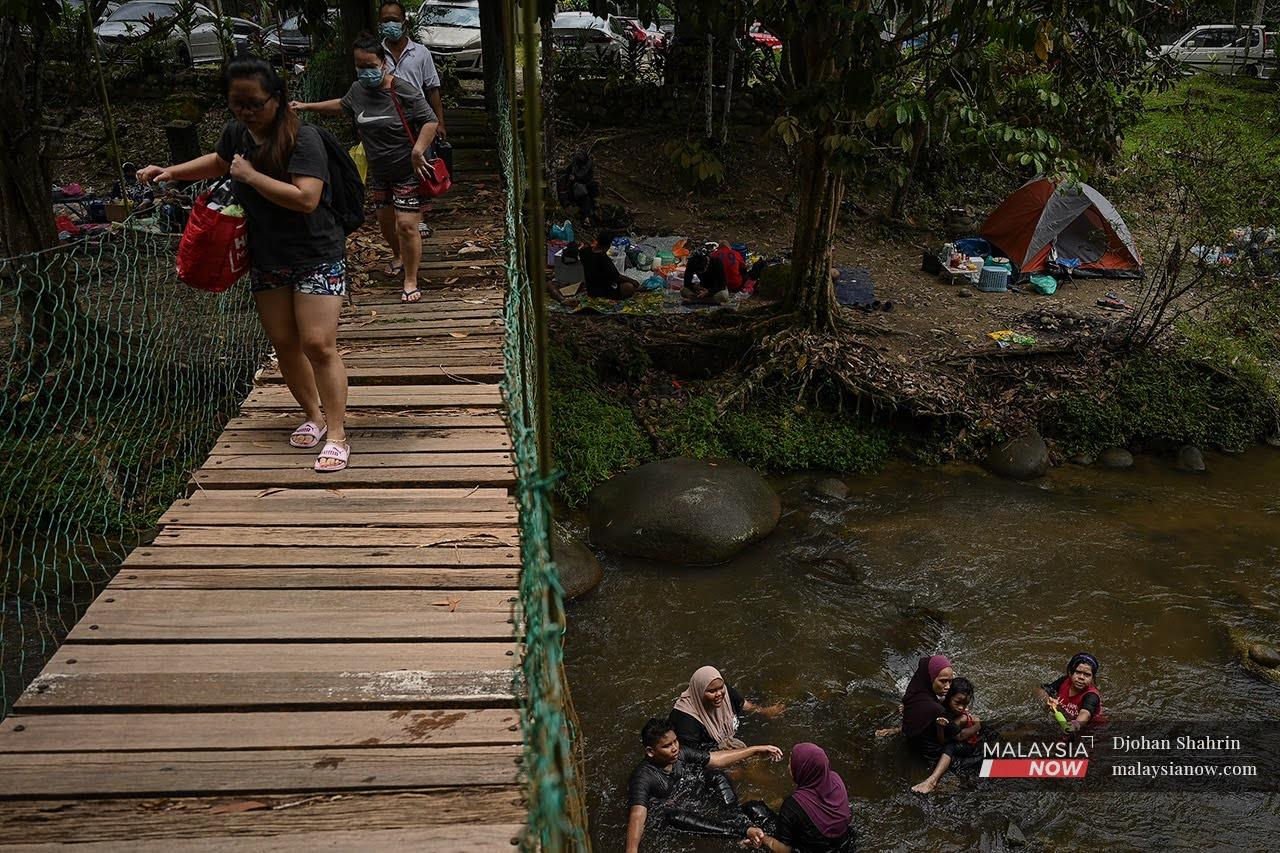 Visitors cross a suspension bridge in Sungai Congkak, Hulu Langat, while others splash about in the river below.