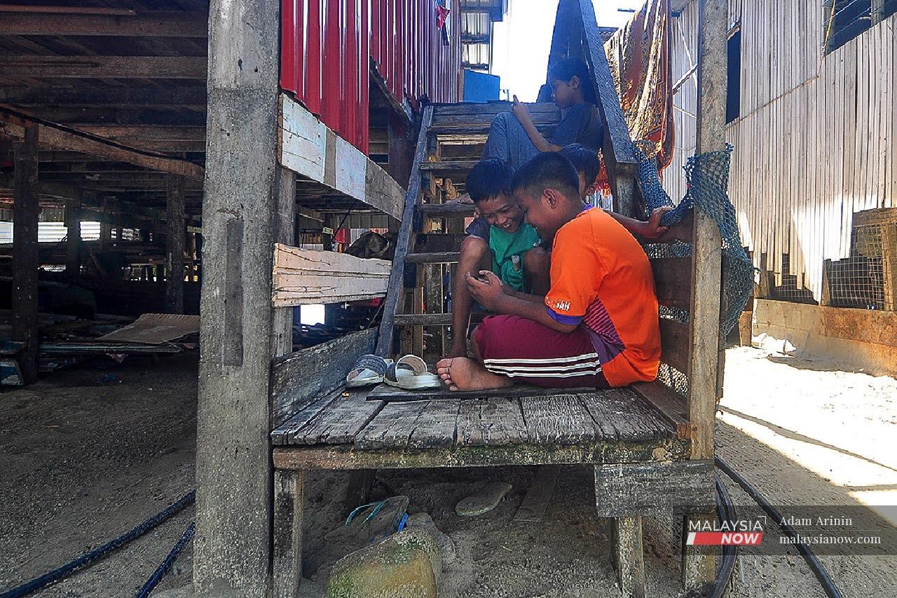 Kanak-kanak menggunakan telefon pintar untuk melayari internet dan bermain permainan video di tangga rumah mereka di Kampung Gaya Asli, Pulau Gaya.