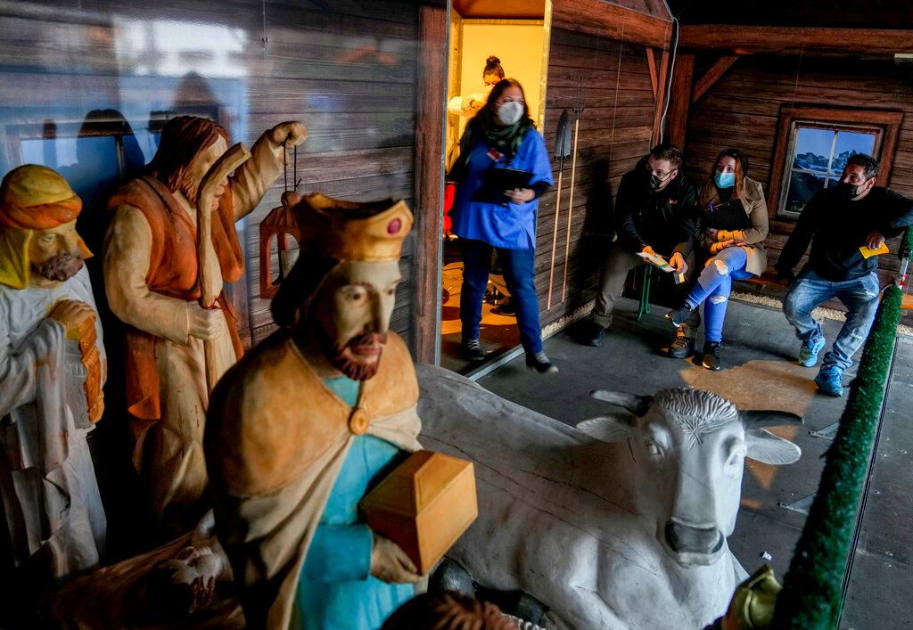 A medical worker and people waiting for a Covid-19 vaccination stand next to a nativity scene at the Christmas market in Offenbach, Frankfurt, Nov 24. The Christmas booth was turned into a temporary vaccination centre, where people queued for hours. Photo: AP