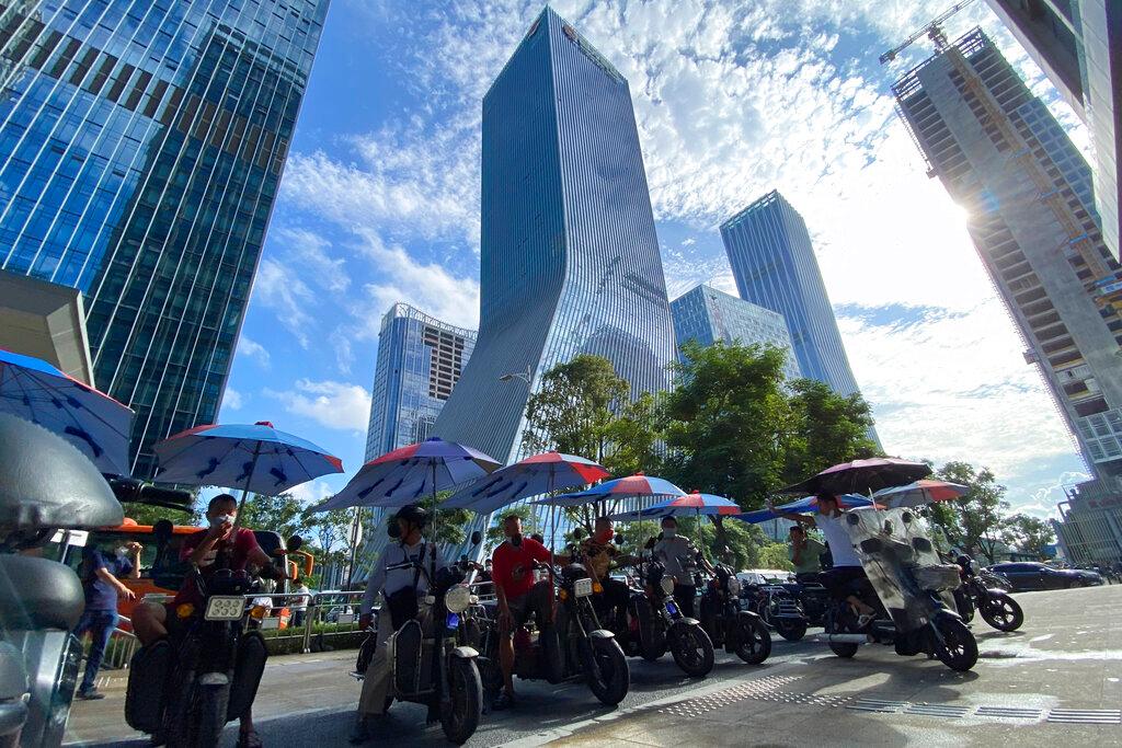 Men on electric bikes wait for riders near the Evergrande headquarters (centre) in Shenzhen, China, Sept 24. Photo: AP