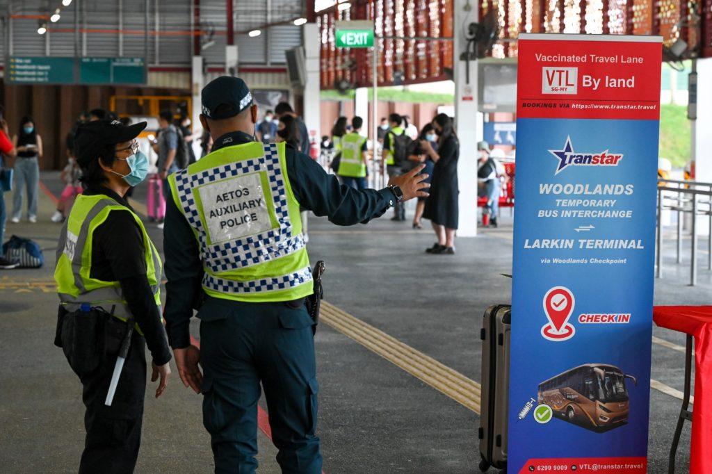 Pihak berkuasa SIangpura memantau pergerakan penumpang yang akan memulakan perjalanan ke Malaysia melalui darat menggunakan bas. Gambar: AFP