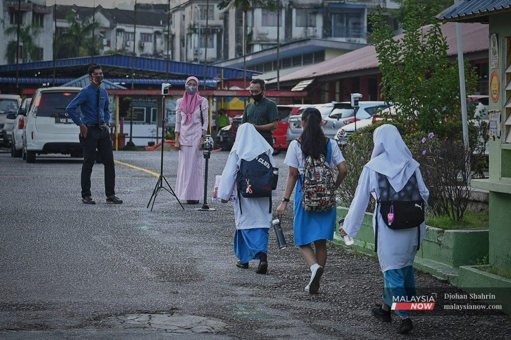 Teachers wait to conduct temperature checks for students at the front gate of a school in the Klang Valley.