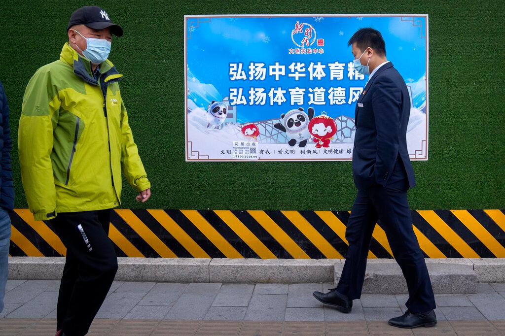 People wearing face masks walk past a poster promoting the 2022 Winter Olympics that reads 'Carry forward the Chinese sports spirit, promote sportsmanship' in Beijing, Dec 8. Photo: AP