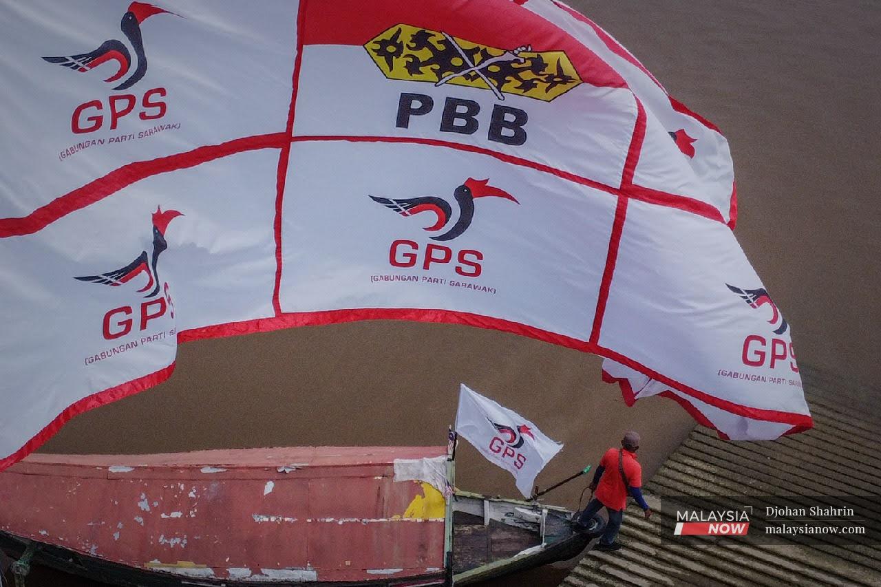 A ferryman steps off his boat and onto the jetty as a giant banner displaying the logos of Gabungan Parti Sarawak and Parti Pesaka Bumiputera Bersatu ripples overhead.