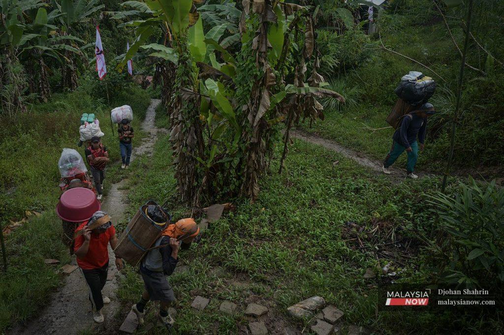 Orang kampung memikul barangan asas ke rumah mereka di kawasan berbukit Kampung Sapit.