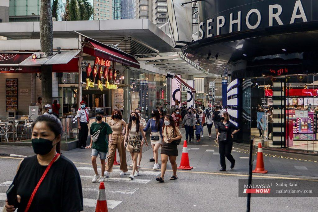 People wearing face masks to curb the spread of Covid-19 cross a street in the shopping district of Bukit Bintang in Kuala Lumpur.