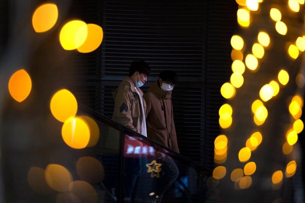People wearing face masks pass by sets of lights at a shopping and office complex in Beijing, Dec 10. Photo: AP