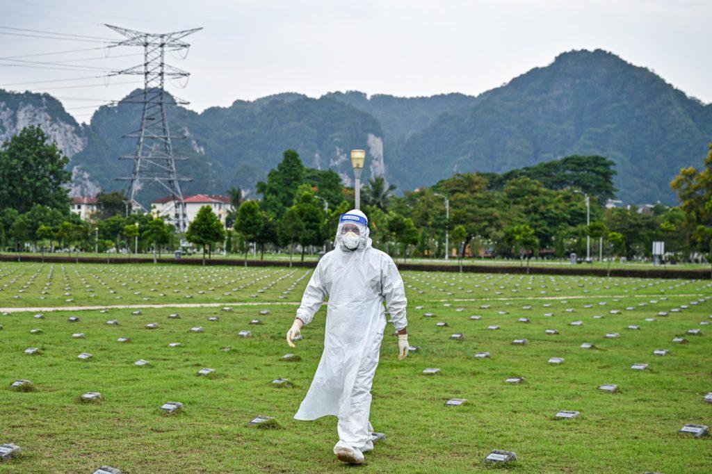 A volunteer wearing personal protective equipment walks past grave markers at a cemetery in Kuala Lumpur in this June 15 file photo. Photo: AFP