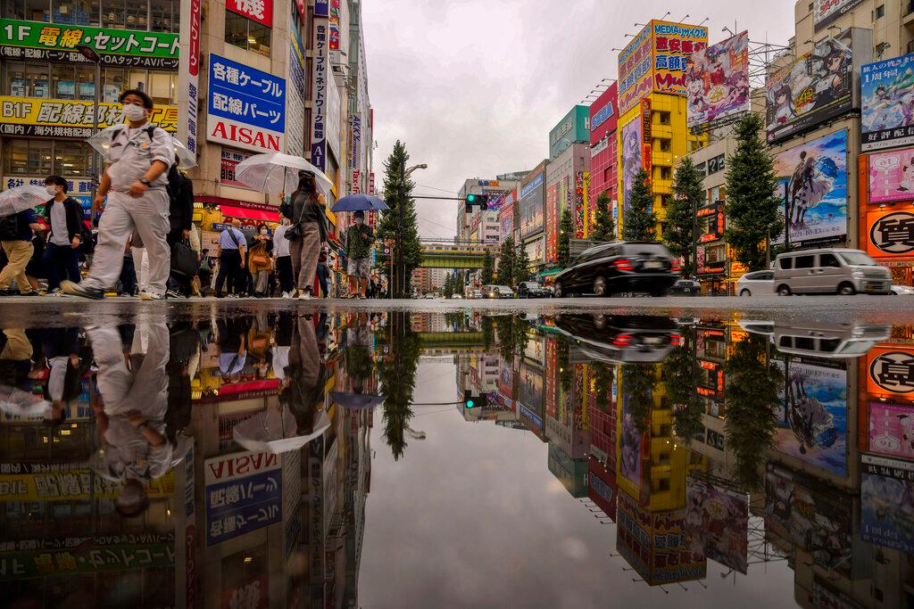 People wearing protective masks are reflected in a puddle as they walk across a street in a shopping district in Tokyo, Oct 12. Photo: AP