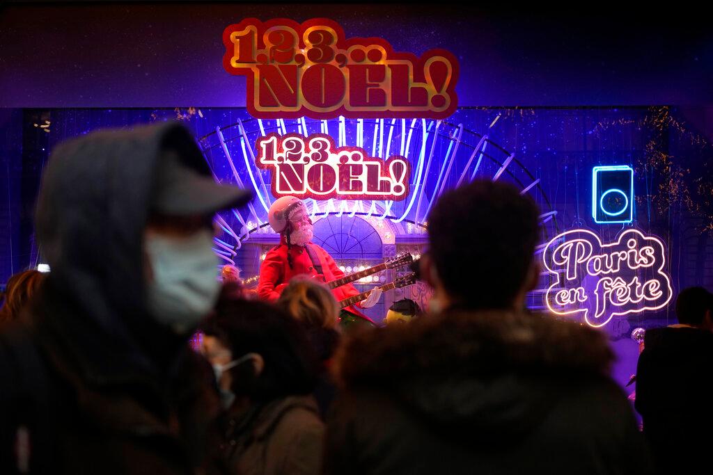 Pedestrians wear masks to prevent the spread of Covid-19 as they walk past a store illuminated as part of Christmas lightings in Paris, Dec 6. Photo: AP