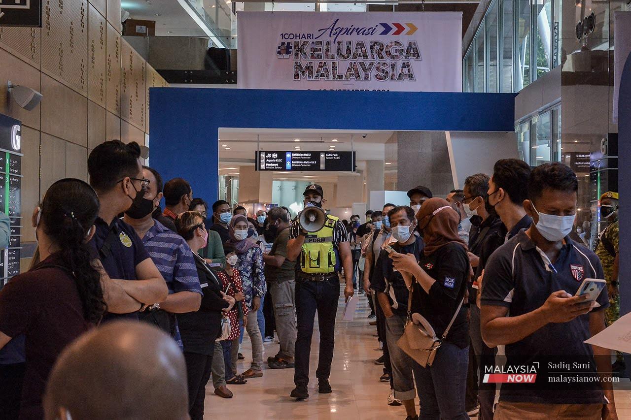 A police officer walks between queues of people lining up for the 80% discount on traffic summonses offered under the 100-Day Aspirasi Keluarga Malaysia Programme at KLCC on Dec 9.