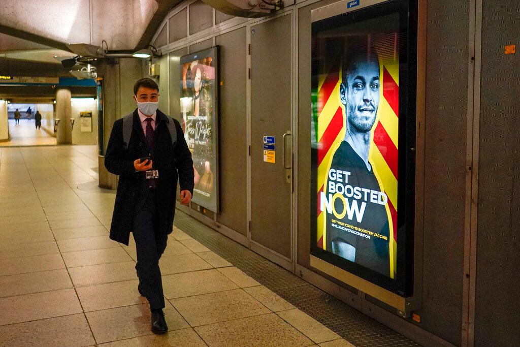 A man wears a face mask as he walks past an advertising in support of the vaccination campaign, in Westminster Station, in London, Dec 16. Photo: AP