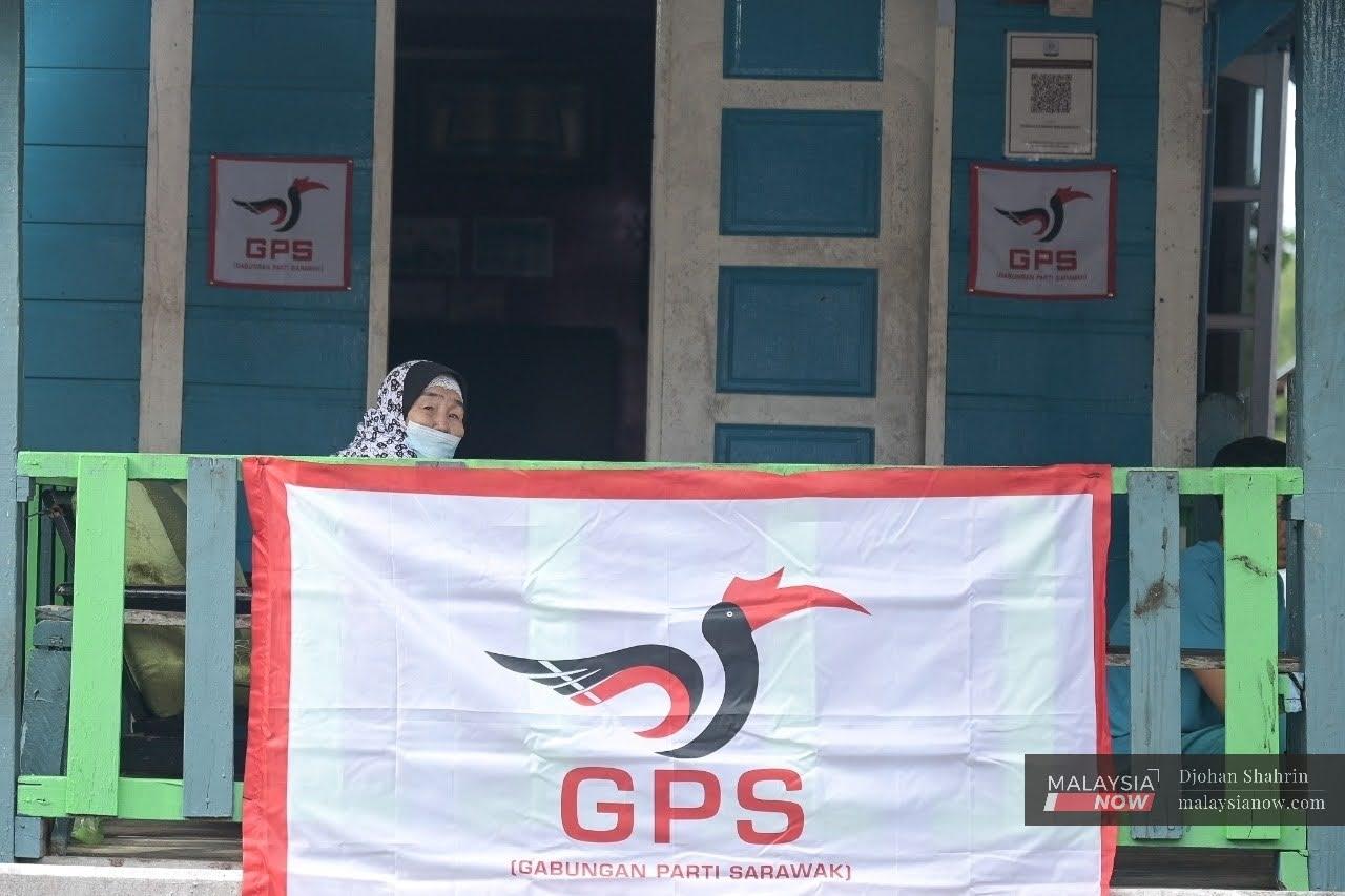 A woman sits outside her house in Pulau Salak, Sarawak, which has been hung with the flags and posters of Gabungan Parti Sarawak.