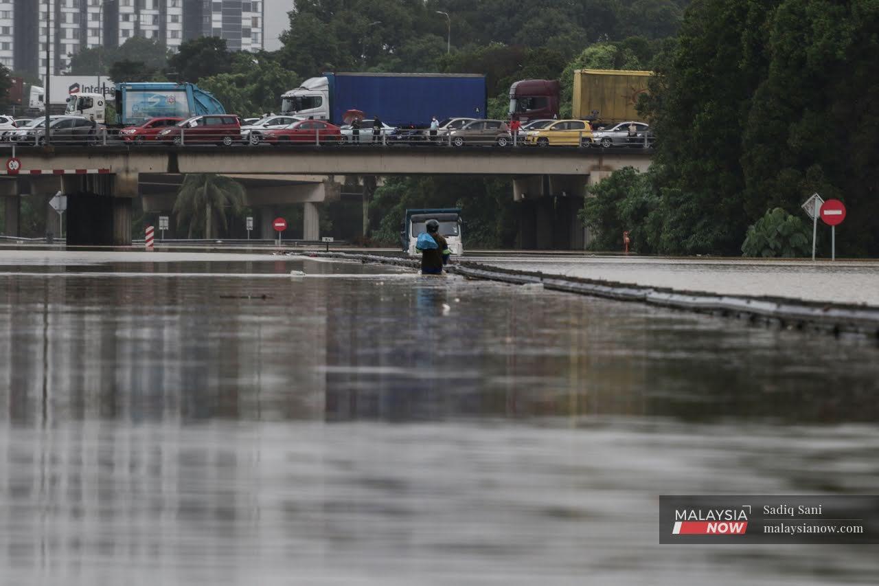 A man wades through flood waters at the NKVE highway in Shah Alam today.