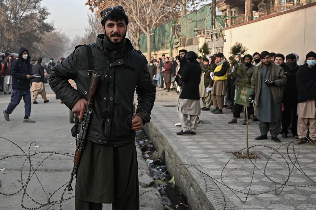 A Taliban fighter stands guard at a checkpoint as people queue to enter the passport office in Kabul on Dec 19, after Afghanistan's Taliban authorities said they would resume issuing passports. Photo: AFP