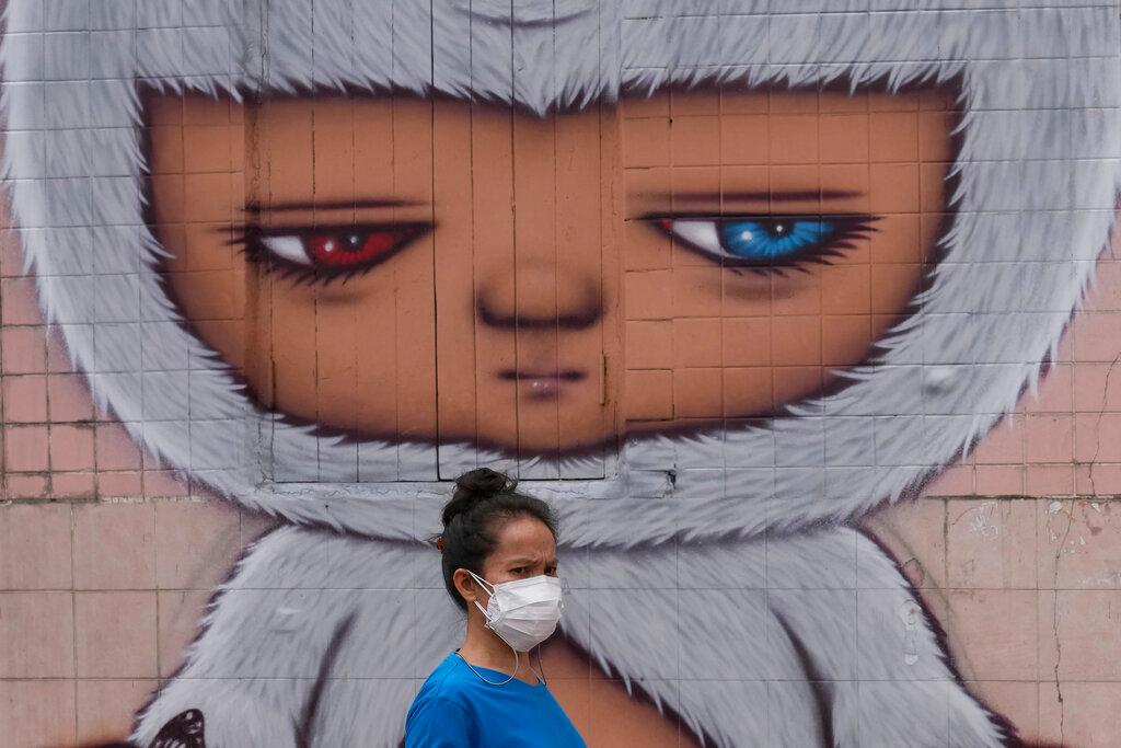 A woman wearing a face mask to help curb the spread of Covid-19 walks past wall art in Bangkok, Thailand, July 20. Photo: AP