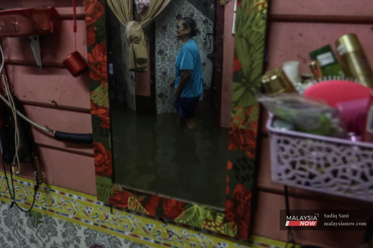 A woman emerges from her room, wading through knee-deep water at her house in Kampung Delek, Klang.