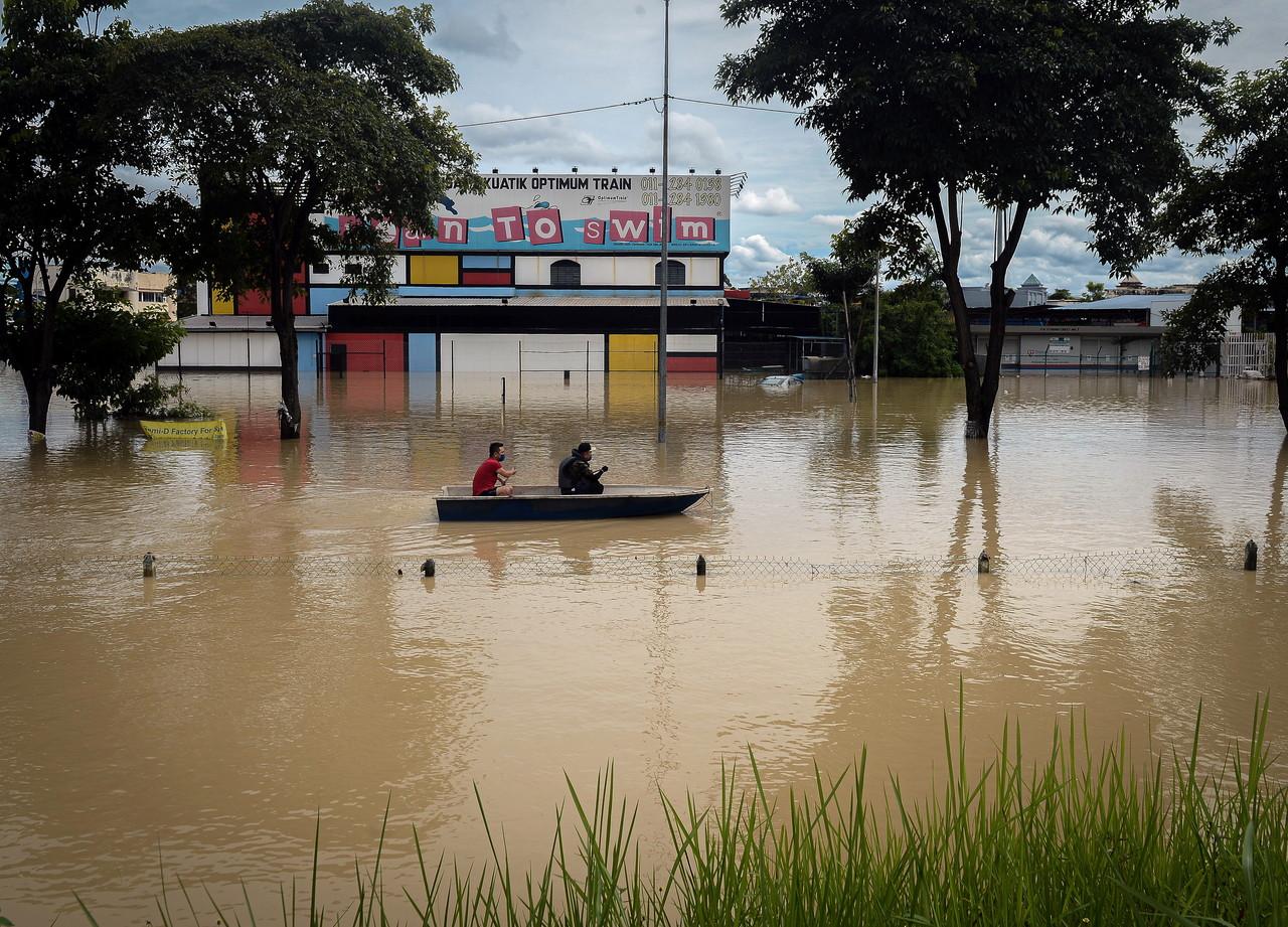 A group of men paddle a boat past a swimming school in Sri Muda, Shah Alam, in search of flood victims in need of aid. Photo: Bernama