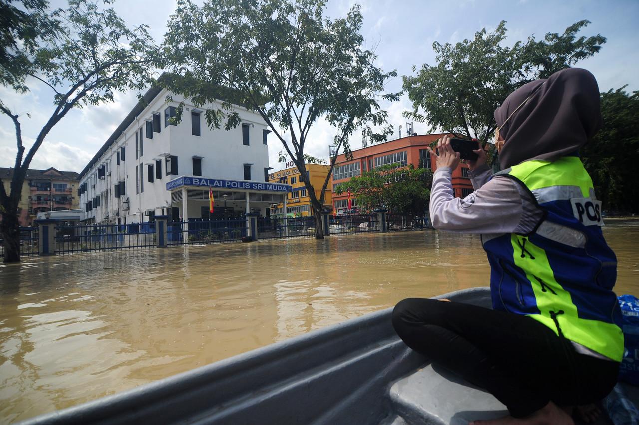 Anggota Polis Lans Kop Nur Fatihah Shari merakam gambar Balai Polis Seri Muda yang ditenggelami air selepas dilanda banjir semasa mengagihkan makanan kepada mangsa banjir ketika tinjauan di Taman Seri Muda Seksyen 25 semalam. Gambar: Bernama