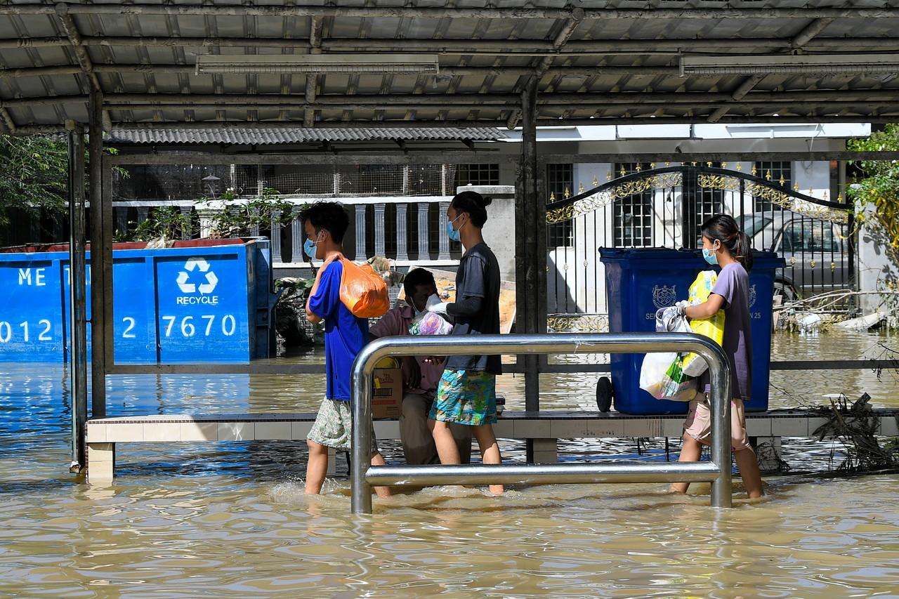 Family members wade through flood waters to collect their belongings in Taman Sri Muda in Section 25, Shah Alam. Photo: Bernama