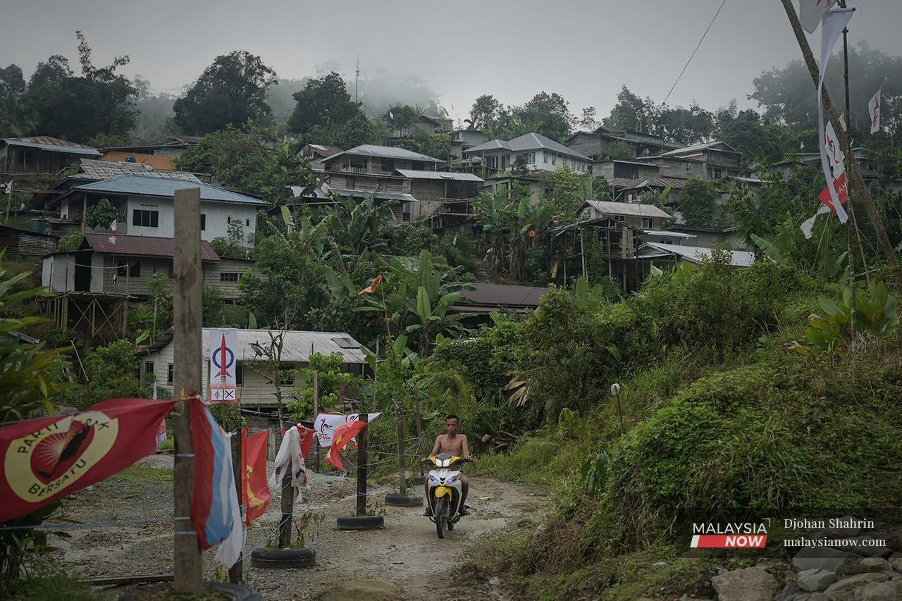 A man rides his motorcycle past a single DAP banner put up amid the flags of other political parties including DAP's fellow Pakatan Harapan component PKR at Kampung Sapit in Sarawak.
