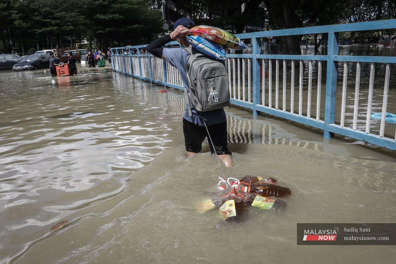 A man carries sacks of rice over his shoulder, pulling bottles of cooking oil behind him as he makes his way through the floodwaters in Taman Sri Muda, Shah Alam.