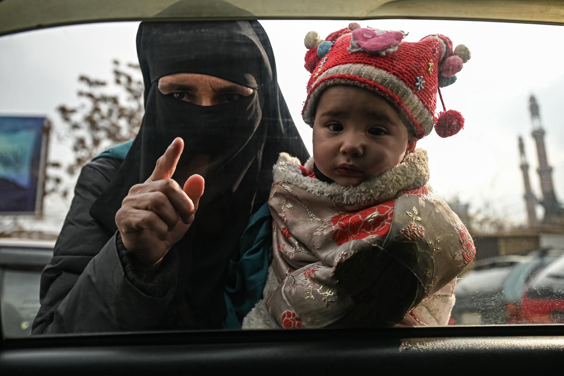 A woman carries a child as she begs from commuters in a car in Kabul on Dec 26. Photo: AFP