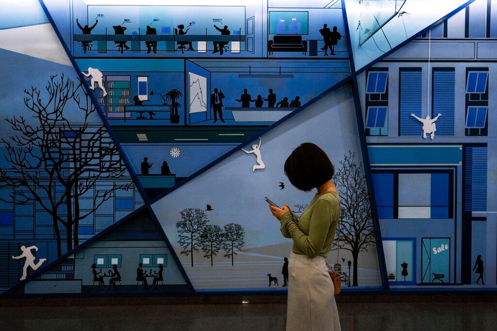 A woman browsing her smartphone in front of a billboard depicting office workers at a subway station in Beijing, Sept 16. Photo: AP