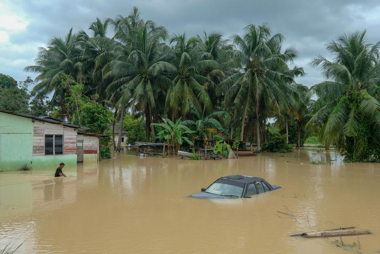 A youth makes his way through waist-deep floodwaters which have partially submerged a car at Kampung Belimbing Dalam, Durian Tunggal in Alor Gajah today. Photo: Bernama