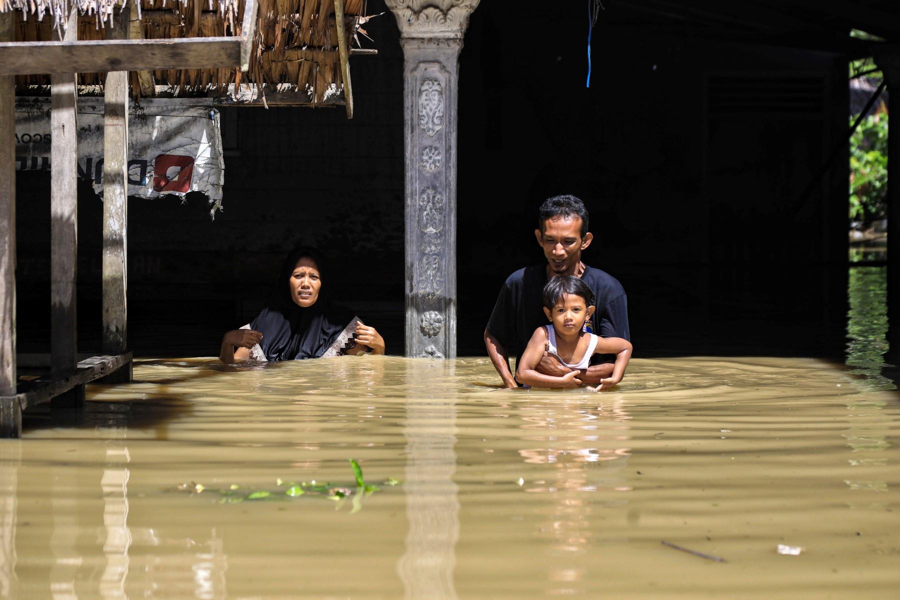 A family wades through floodwaters outside a residence in the Gampong Meunasah area in North Aceh on Jan 4. Photo: AFP