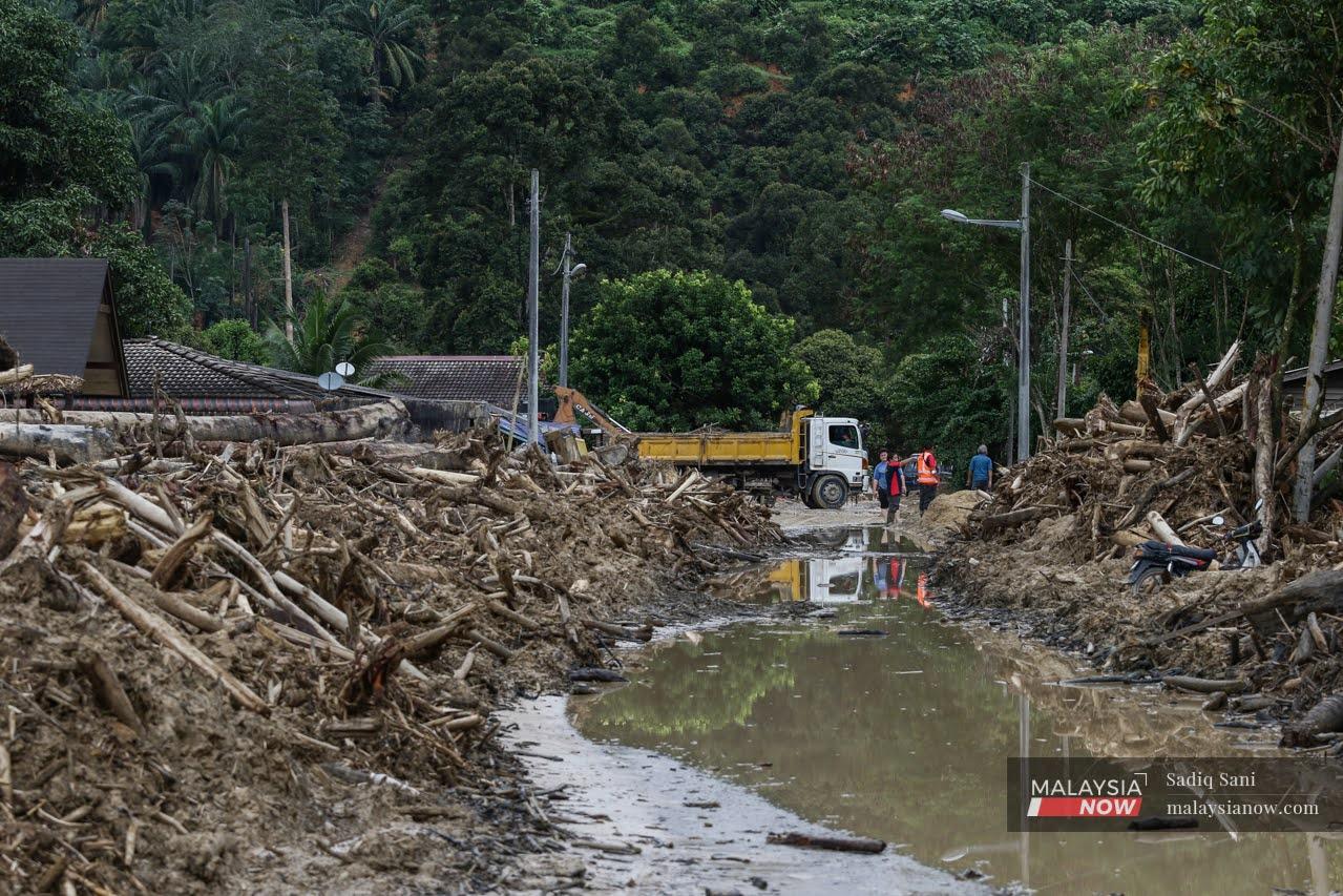 Workers attempt to clear a path through the piles of broken branches and logs washed down by the floods in Kampung Batu 19 in Karak.