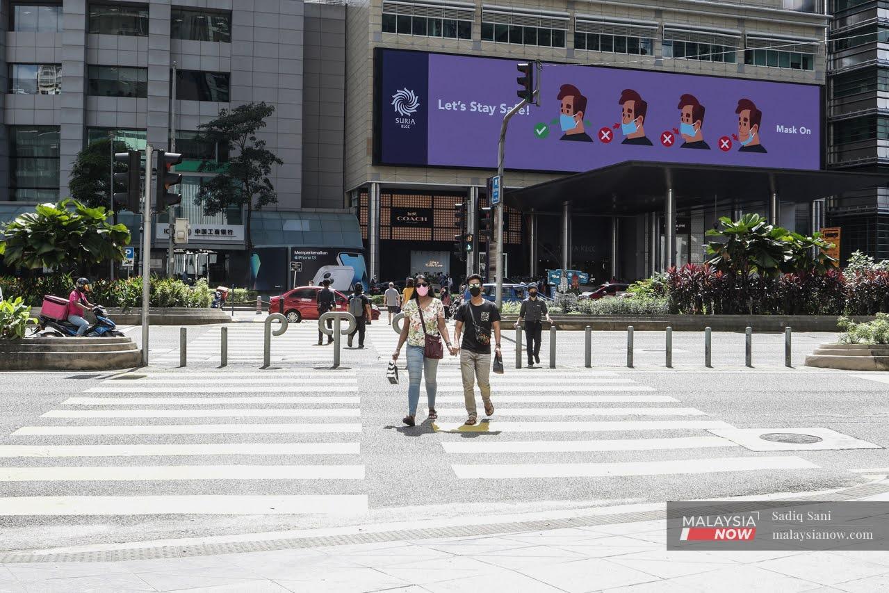People cross a road in Jalan Ampang, Kuala Lumpur, near a digital billboard reminding the public of the proper way to wear a face mask.