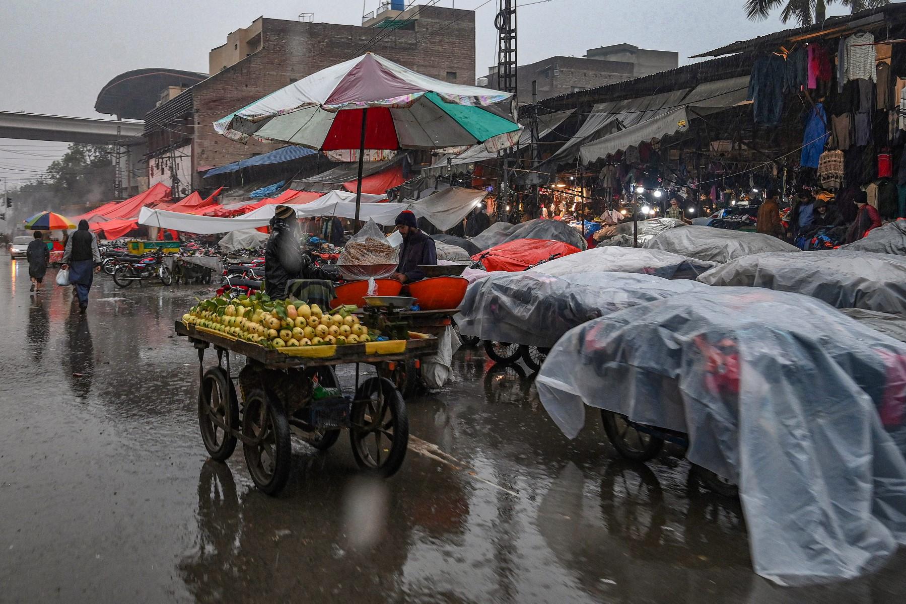 Street vendors use plastic sheets to cover their carts as it rains in Lahore on Jan 5. Photo: AFP