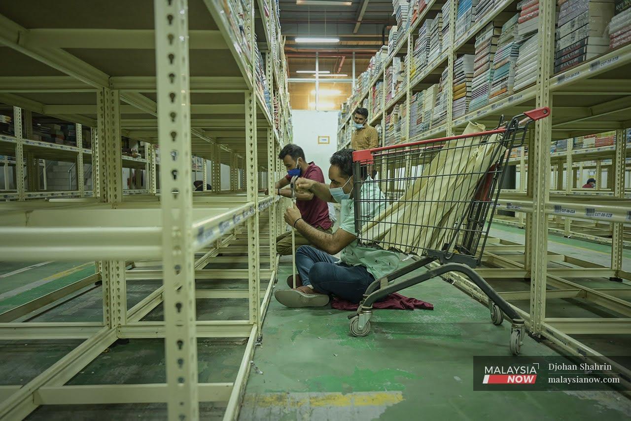 Pekerja BookXcess melakukan kerja-kerja membaiki dan pembersihan rak buku di dalam gudang yang dilanda banjir hingga mengakibat jutaan buku rosak di Seksyen 33, Shah Alam.
