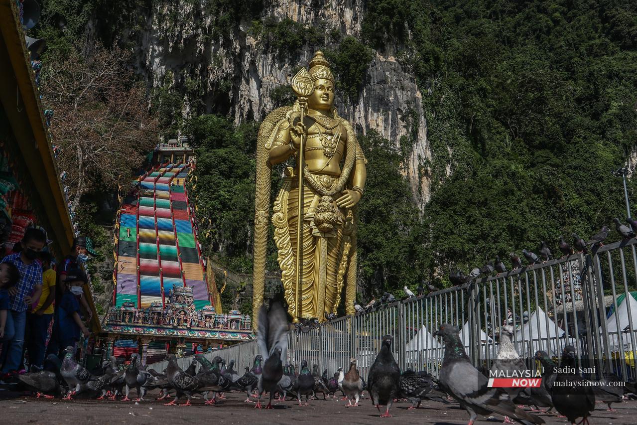 A flock of pigeons peck at food on the ground in front of the statue of Lord Murugan at the Sri Subramaniam Temple in Batu Caves, Selangor.