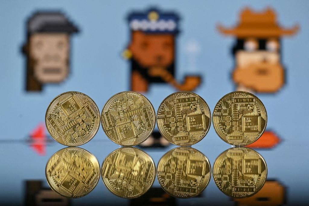 An illustration picture taken in London on Dec 30, 2021, shows gold-plated souvenir cryptocurrency coins arranged beside a screen displaying a NFT (non-fungible token) marketplace. NFTs are cryptographic assets stored on a blockchain with unique identification metadata that distinguish them from each other. Photo: AFP