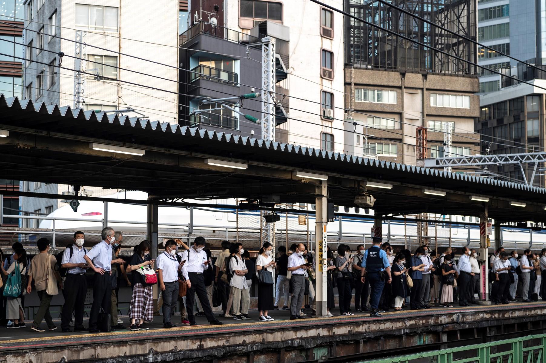 People stand on the platform as they wait for their train at a station in Tokyo on July 28, 2021. Photo: AFP