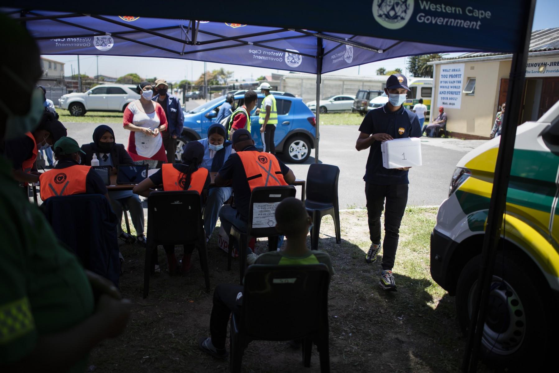 People register before getting vaccinated outside an ambulance which has been converted to facilitate vaccinations at a Covid-19 vaccination event in Manenberg, which is part of the Vaxi-Taxi mobile vaccination drive, on Dec 08, 2021 in Cape Town. Photo: AFP
