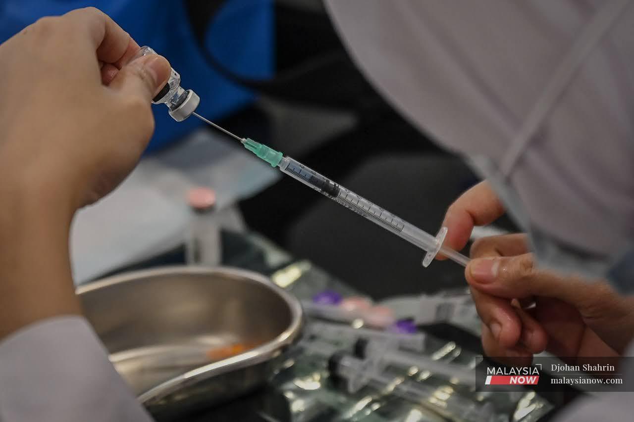 Petugas kesihatan membuat persiapan vaksin pada picagari sebelum melakukan vaksinasi.