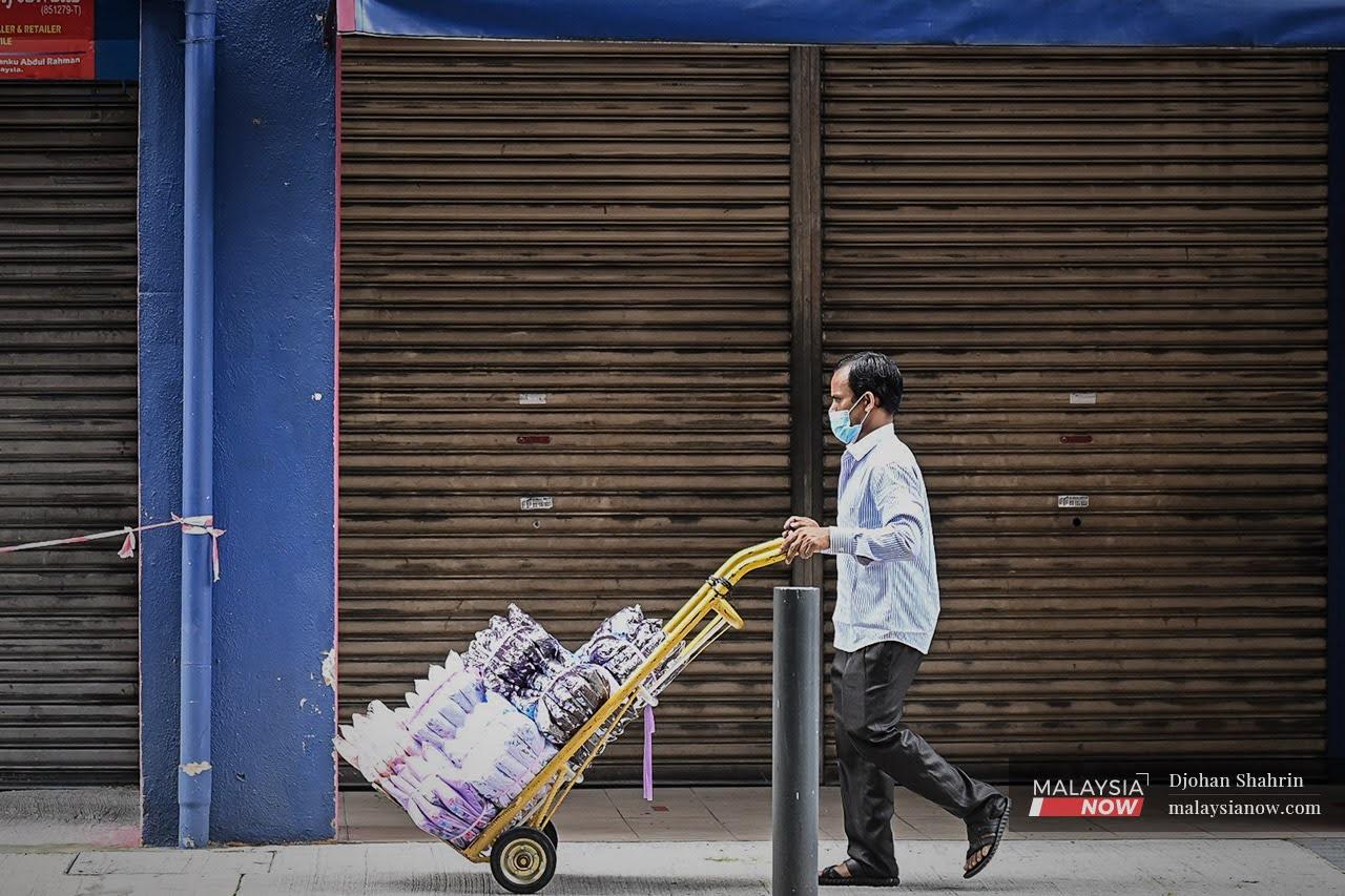 A worker pushes a trolley past a row of closed shops in Jalan Tuanku Abdul Rahman, Kuala Lumpur.