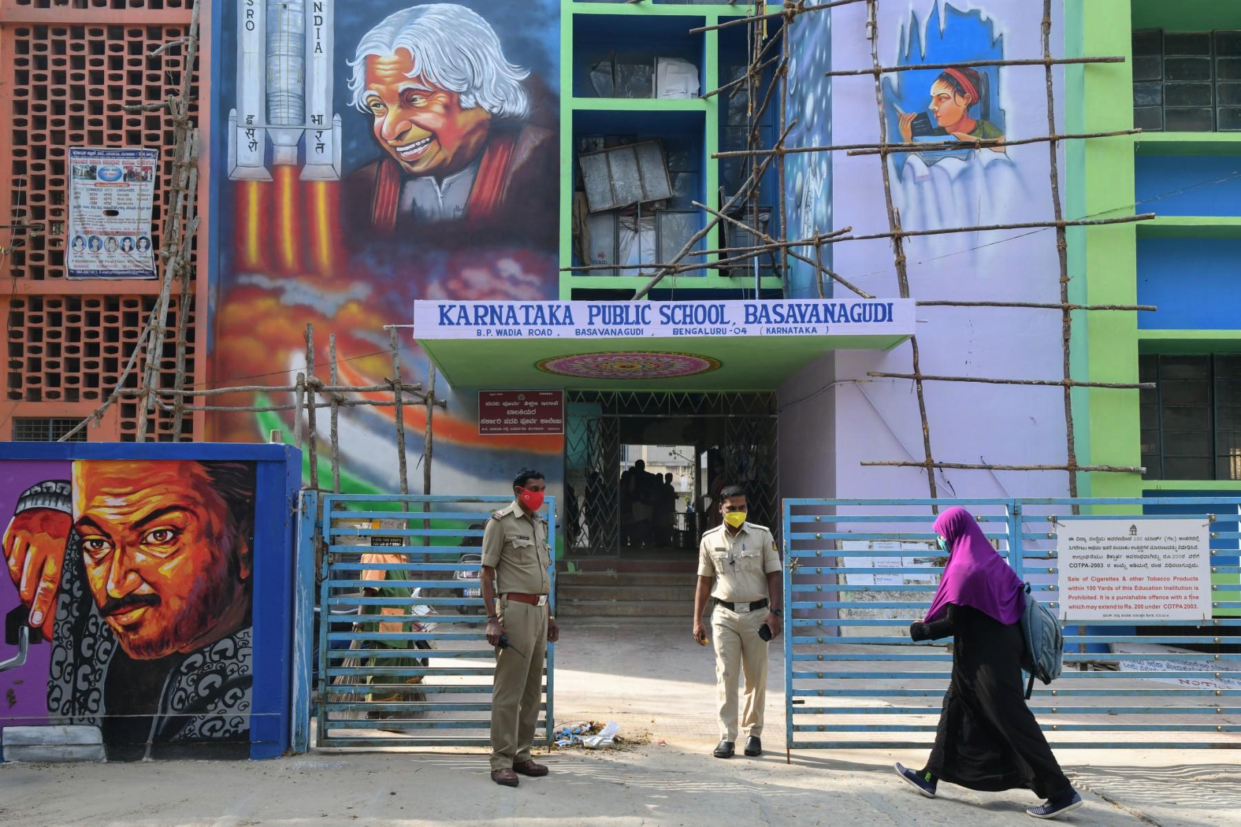Police stand guard as a student of a government high school and pre-university college for women enters the premises of the educational institute in Bangalore on Feb 16, after schools reopened in southern India under tight security after authorities banned public gatherings following protests over Muslim girls wearing the hijab in classrooms. Photo: AFP
