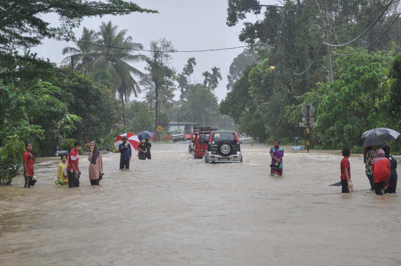 People stand knee-deep in water as floods cover the road near Kampung Darau in Besut, Terengganu. Photo: Bernama