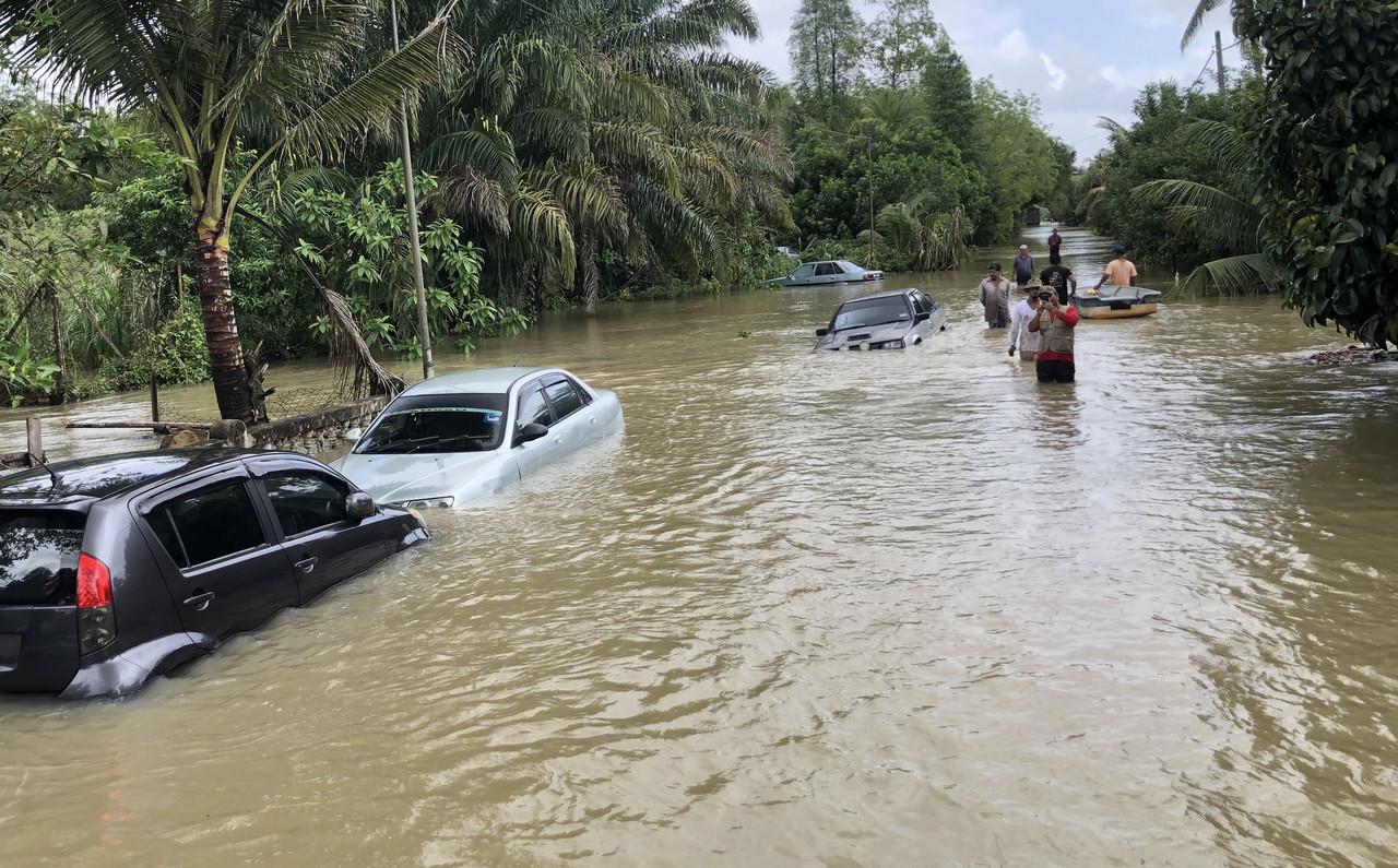 Cars lie half-submerged in floodwater as people wade by in Kampung Tok Sangkut, Pasir Mas in Kelantan on Feb 28. Photo: Bernama