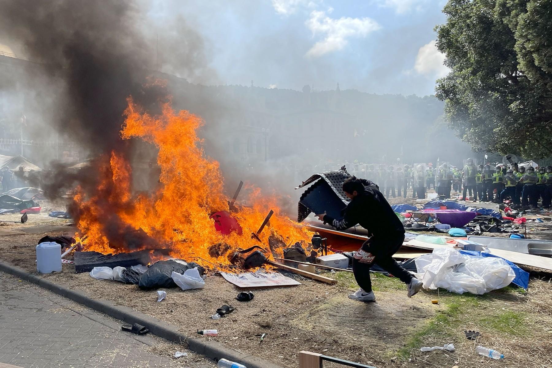 A man throws plastic onto the fire as police move in to clear protesters from Parliament grounds in Wellington on March 2, during demonstrations against Covid-19 vaccine mandates and restrictions. Photo: AFP