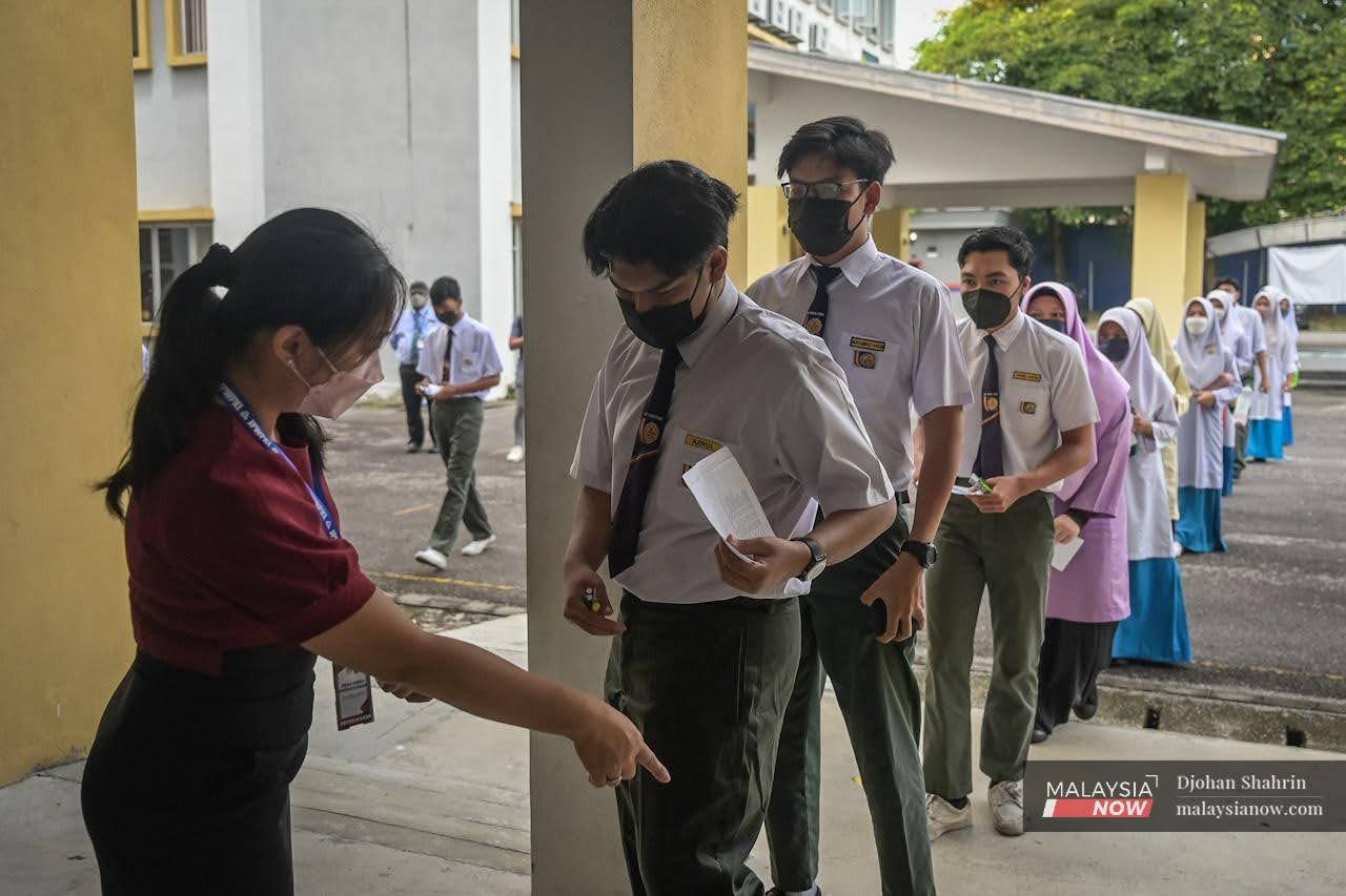 Seorang pengawas peperiksaan memeriksa pelajar-pelajar Sekolah Menengah Kebangsaan Sentul Utama yang berbaris untuk masuk ke dewan peperiksaan Sijil Pelajaran Malaysia 2021 hari ini.
