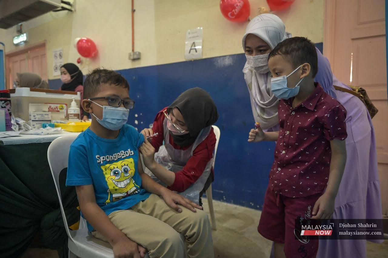 Seorang kanak-kanak tenang ditemani ibunya ketika menerima vaksin PPV Dewan Komuniti Taman Bukit Mewah, Kajang.