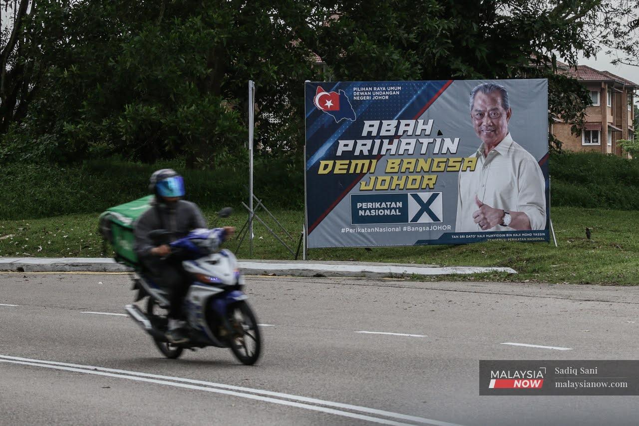 A motorcyclist drives past a billboard featuring Perikatan Nasional chairman and Gambir assemblyman Muhyiddin Yassin in Stulang, Johor.