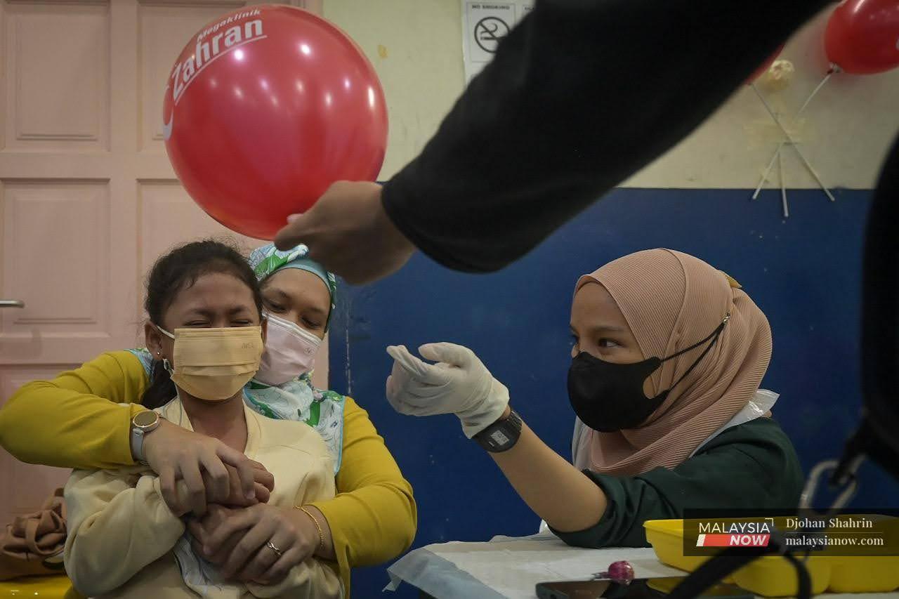 Gelagat seorang kanak-kanak ketika petugas kesihatan dari Megaklinik Zahran mahu memberi vaksin kepadanya pada Program Imunisasi Covid-19 Kanak-Kanak (PICKids) di PPV Dewan Komuniti Taman Bukit Mewah, Kajang.